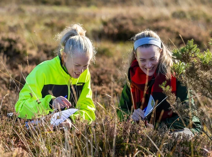 Two women comparing bog plants with a plant identification worksheet